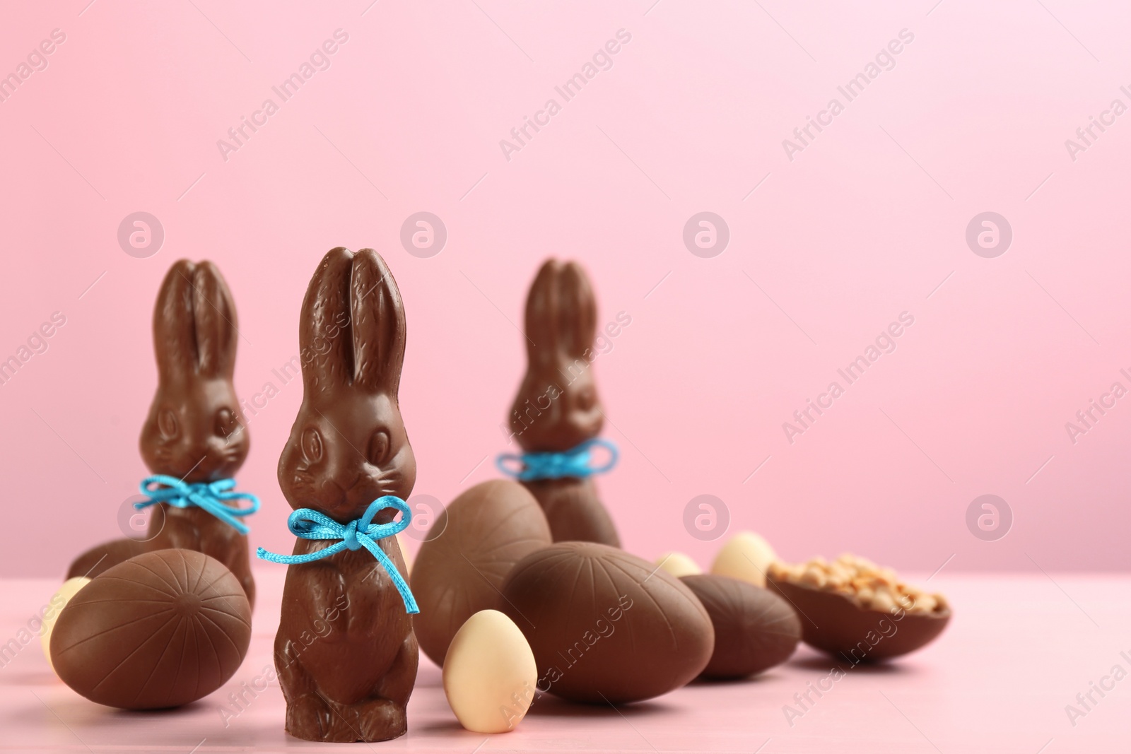 Photo of Chocolate Easter bunnies with bows and eggs on pink wooden table. Space for text