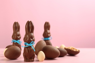 Photo of Chocolate Easter bunnies with bows and eggs on pink wooden table. Space for text