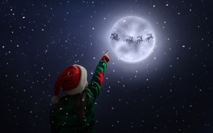 Cute little girl looking at Santa Claus with reindeers in sky on full moon night. Christmas holiday