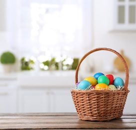 Image of Colorful Easter eggs in wicker basket on wooden table indoors, space for text 