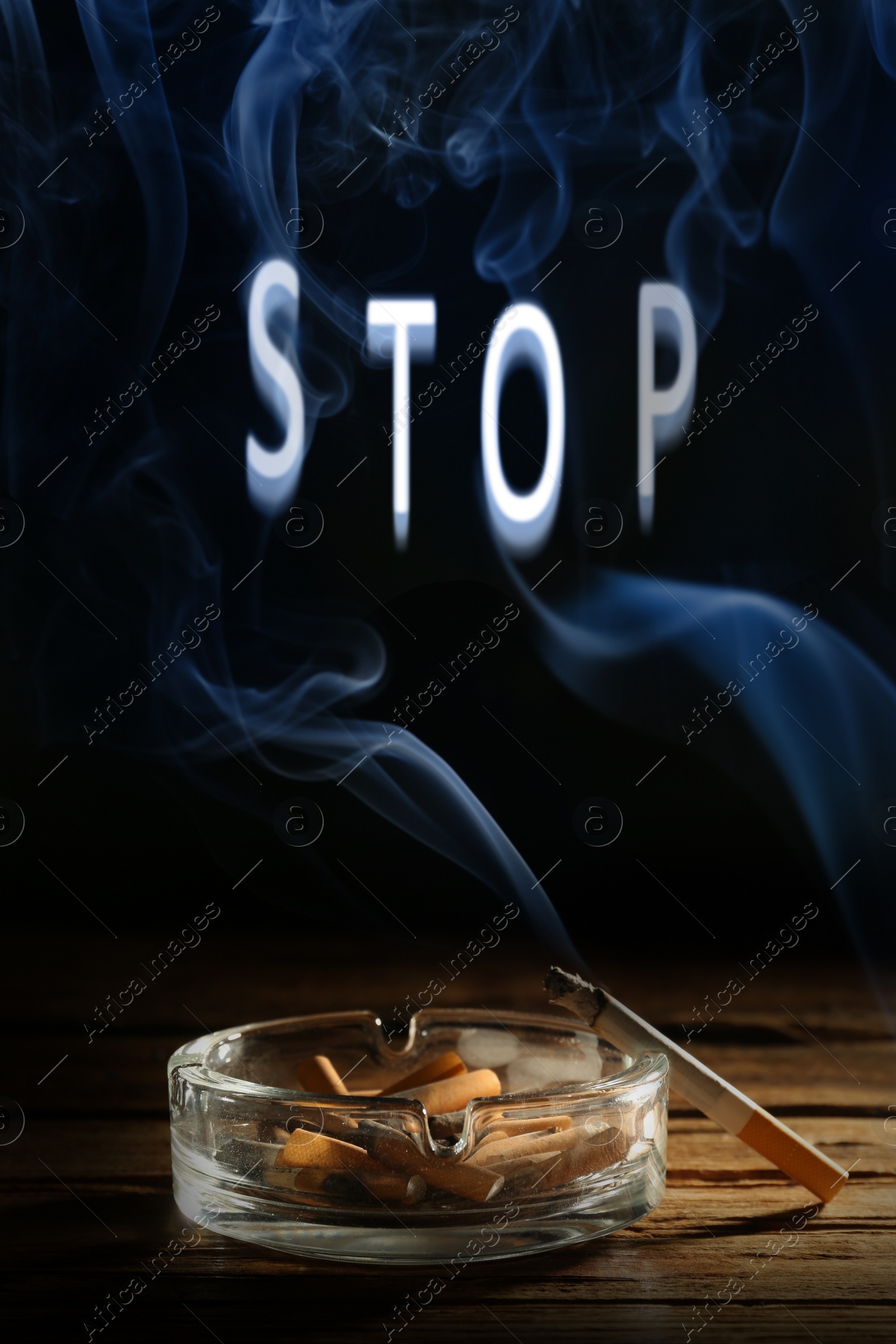 Image of Quit smoking. Word Stop of smoke, ashtray with stubs and smoldering cigarette on wooden table against black background