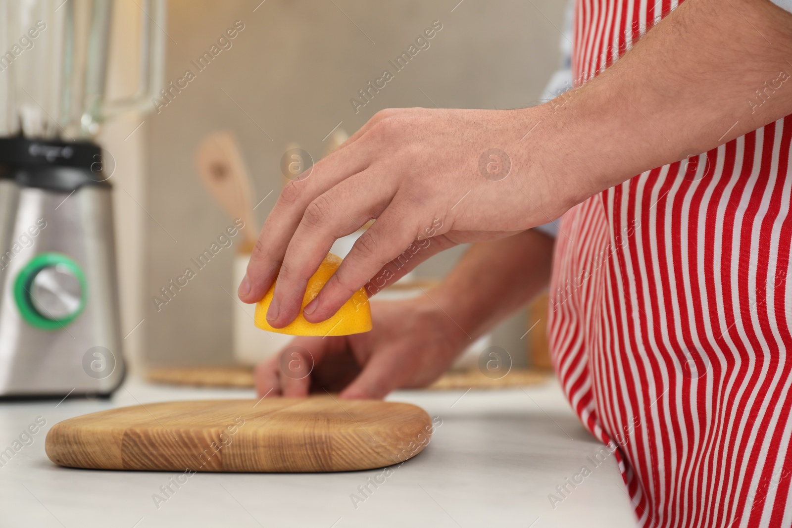 Photo of Man applying lemon juice on wooden cutting board at light table in kitchen, closeup