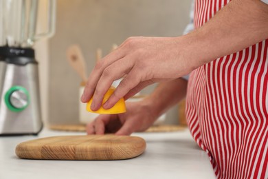 Man applying lemon juice on wooden cutting board at light table in kitchen, closeup