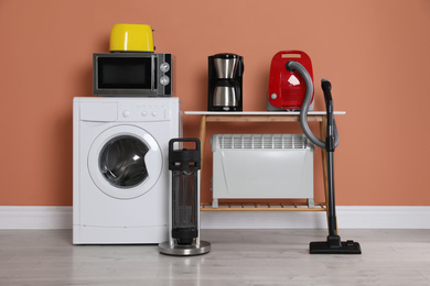 Photo of Set of different home appliances with vacuum cleaner near brown wall indoors