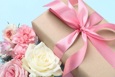 Photo of Gift box and beautiful flowers on light blue background, closeup