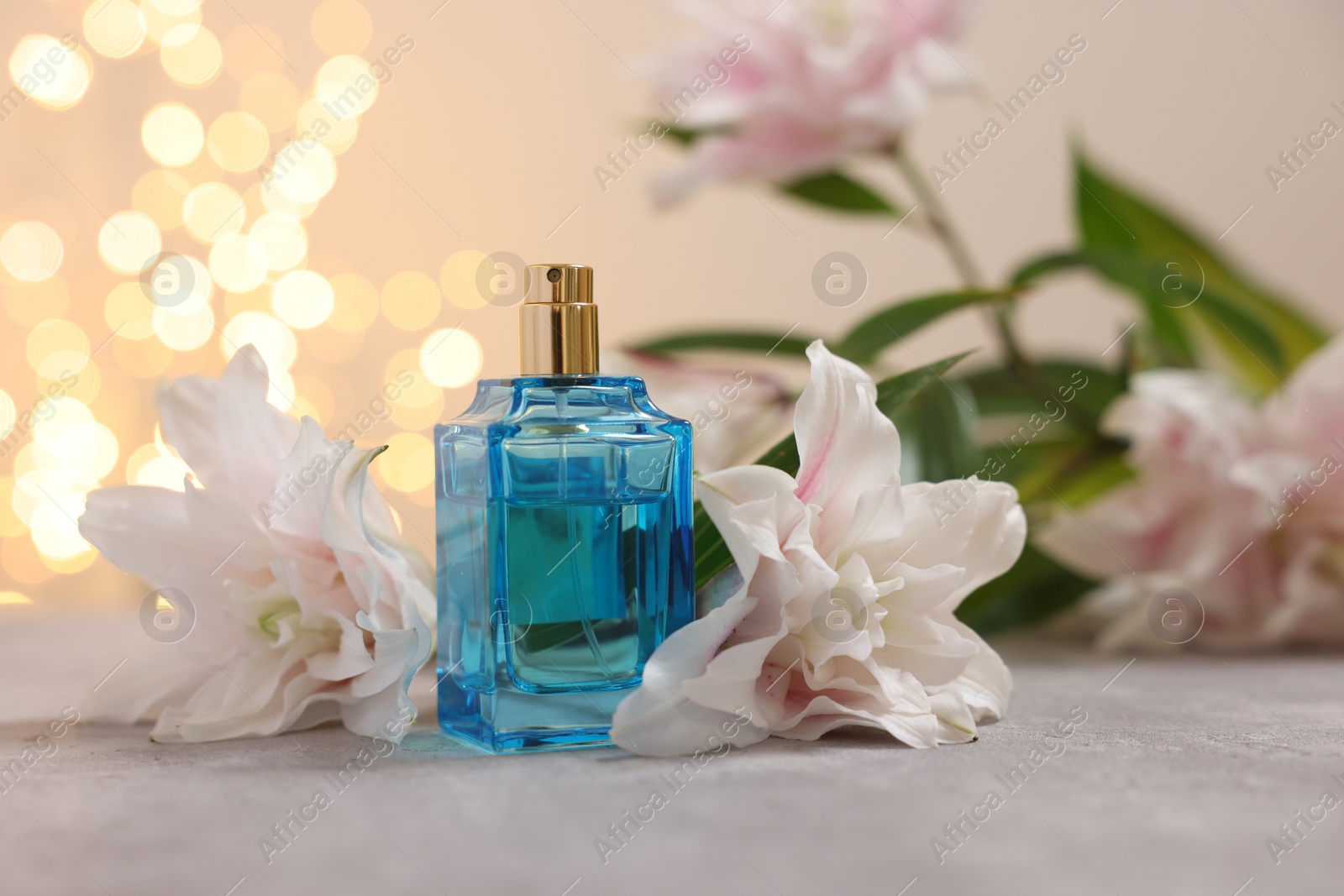 Photo of Bottle of perfume and beautiful lily flowers on table against beige background with blurred lights, closeup