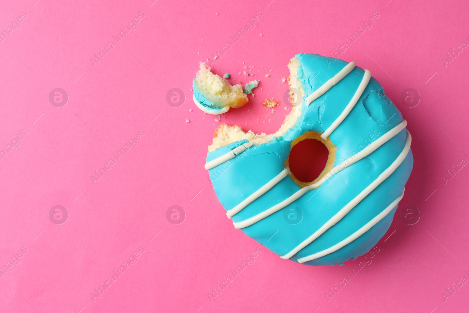 Photo of Sweet bitten glazed donut on pink background, top view. Space for text