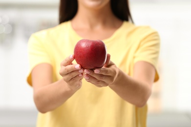 Photo of Woman holding ripe red apple in kitchen, closeup