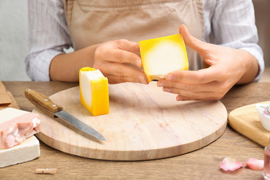Woman holding natural handmade soap at wooden table, closeup