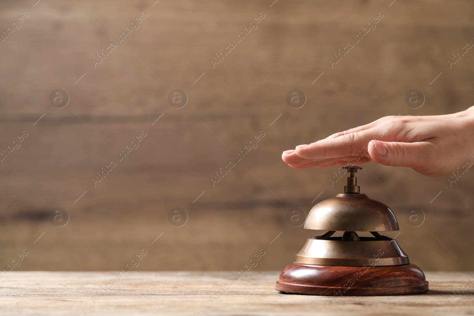 Photo of Woman ringing hotel service bell at wooden table, closeup. Space for text