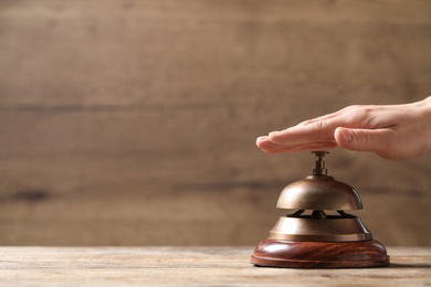 Photo of Woman ringing hotel service bell at wooden table, closeup. Space for text