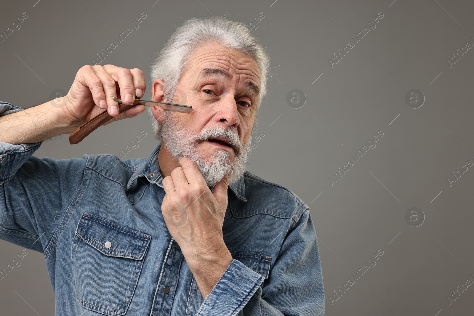 Photo of Senior man shaving beard with blade on grey background, space for text