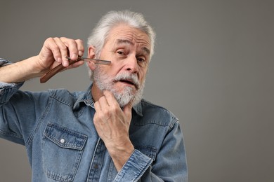 Senior man shaving beard with blade on grey background, space for text