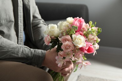 Photo of Man holding bouquet of beautiful flowers indoors, closeup