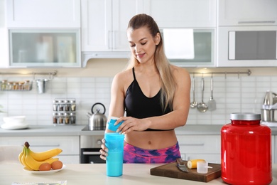 Photo of Young woman preparing protein shake at table in kitchen