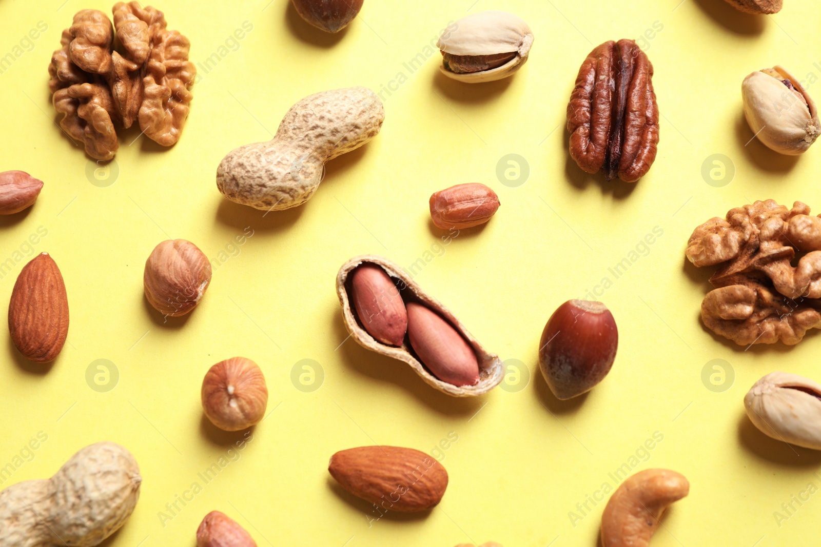 Photo of Different delicious nuts on yellow background, flat lay