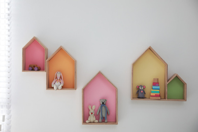 Photo of Colorful house shaped shelves on white wall indoors. Children's room interior design
