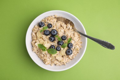 Photo of Tasty oatmeal with blueberries, mint and almond petals in bowl on light green background, top view