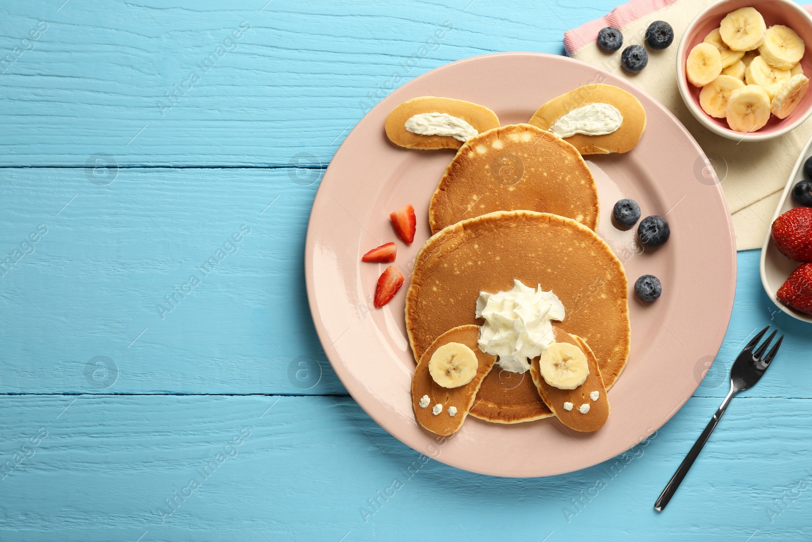 Photo of Creative serving for kids. Plate with cute bunny made of pancakes, berries, cream and banana on light blue wooden table, flat lay. Space for text