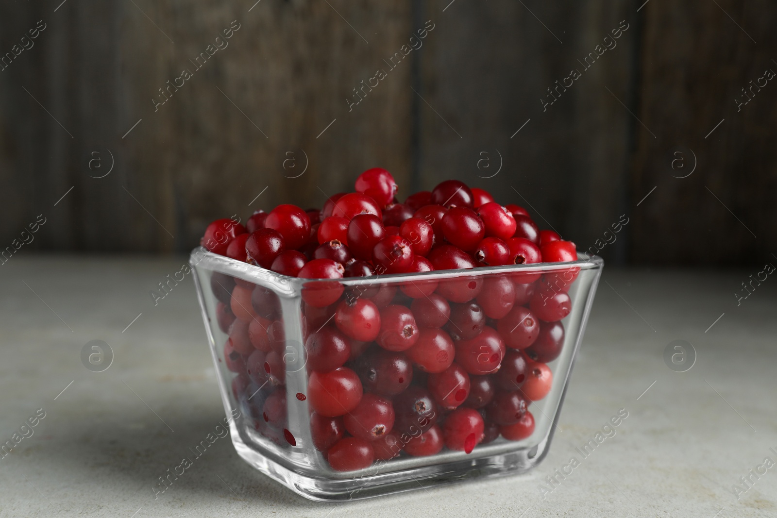 Photo of Cranberries in bowl on light grey table, closeup