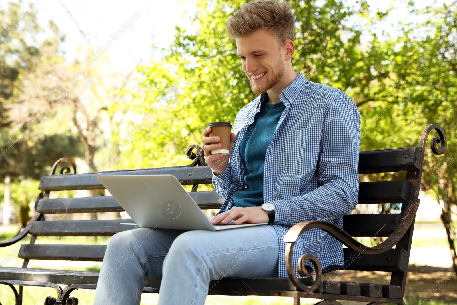 Image of Young man with paper cup of coffee working on laptop in park