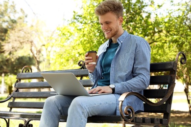 Image of Young man with paper cup of coffee working on laptop in park