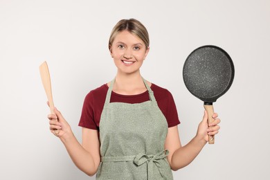 Photo of Beautiful young woman in clean apron with kitchen tools on light grey background