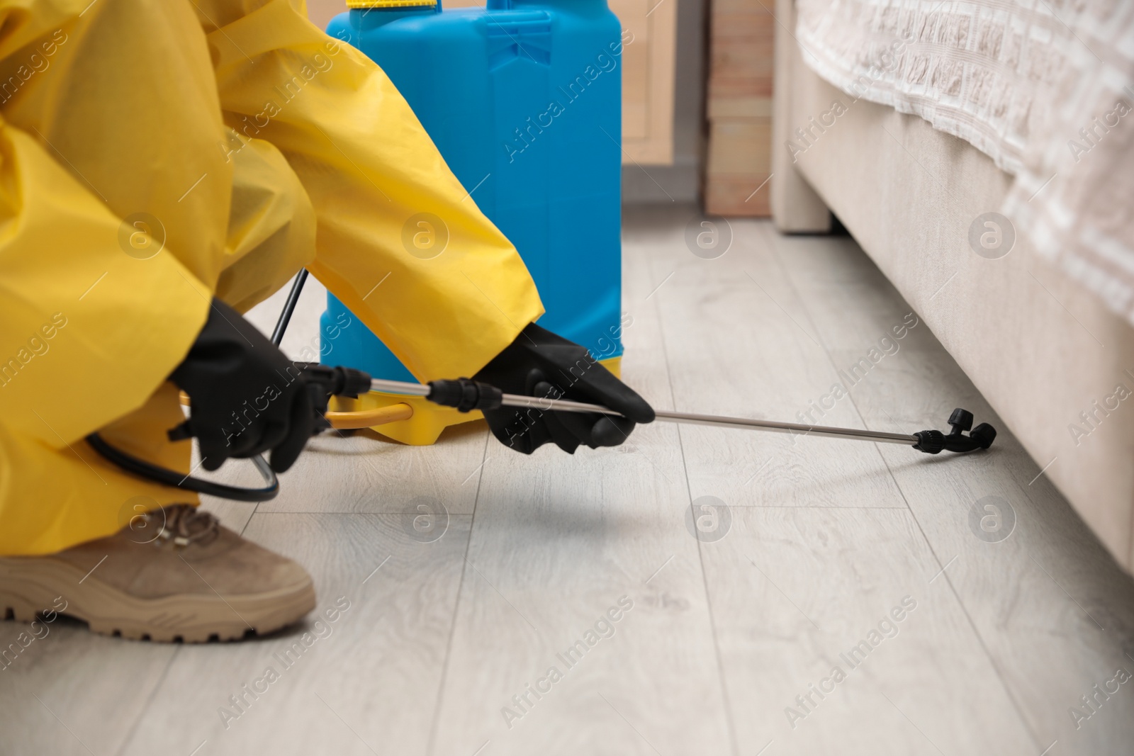 Photo of Pest control worker spraying pesticide under furniture indoors, closeup