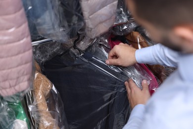 Photo of Dry-cleaning service. Worker taking jacket from rack indoors, closeup
