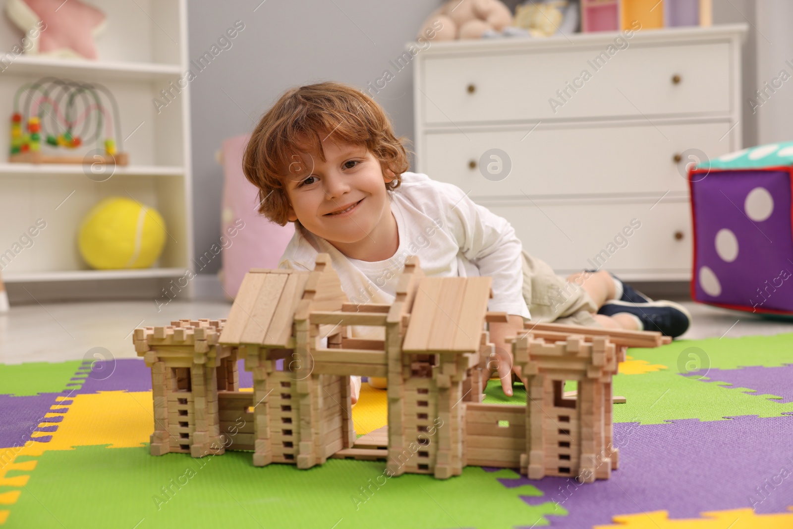 Photo of Little boy playing with wooden entry gate on puzzle mat in room. Child's toy