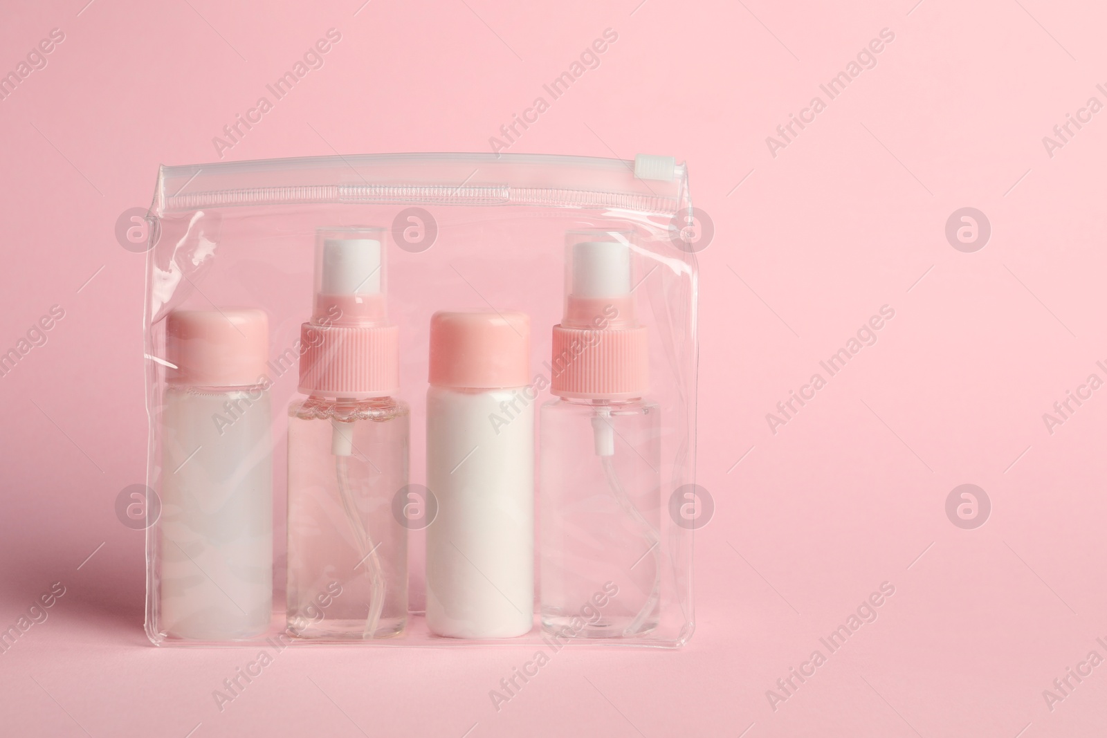 Photo of Cosmetic travel kit in plastic bag on pink background. Space for text