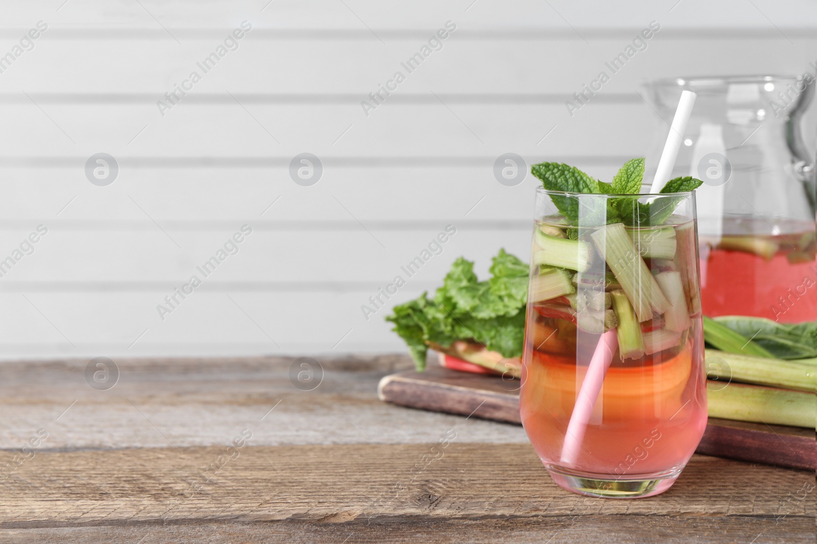 Photo of Glass and jug of tasty rhubarb cocktail on wooden table, space for text