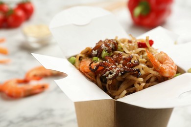 Photo of Box of wok noodles with seafood on light  table, closeup