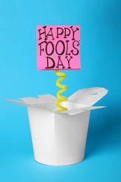 Photo of Lunch box with Happy Fools' Day note on light blue background