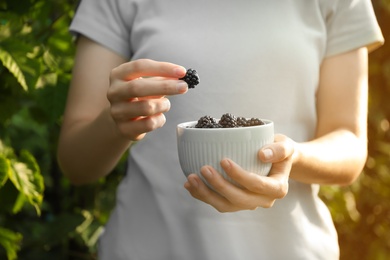 Woman with bowl of tasty ripe blackberries in garden, closeup