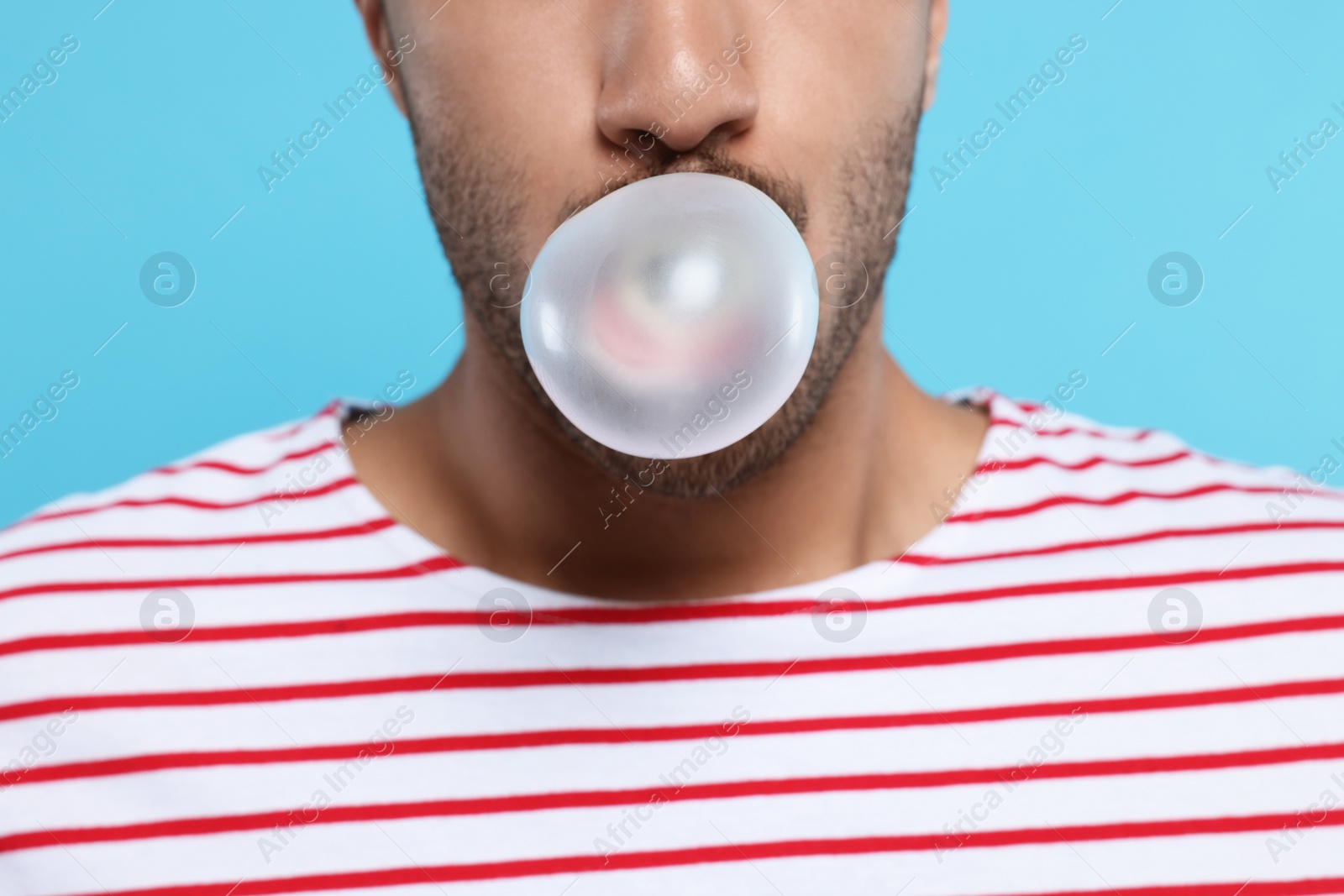 Photo of Man blowing bubble gum on light blue background, closeup