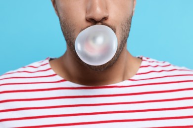 Man blowing bubble gum on light blue background, closeup