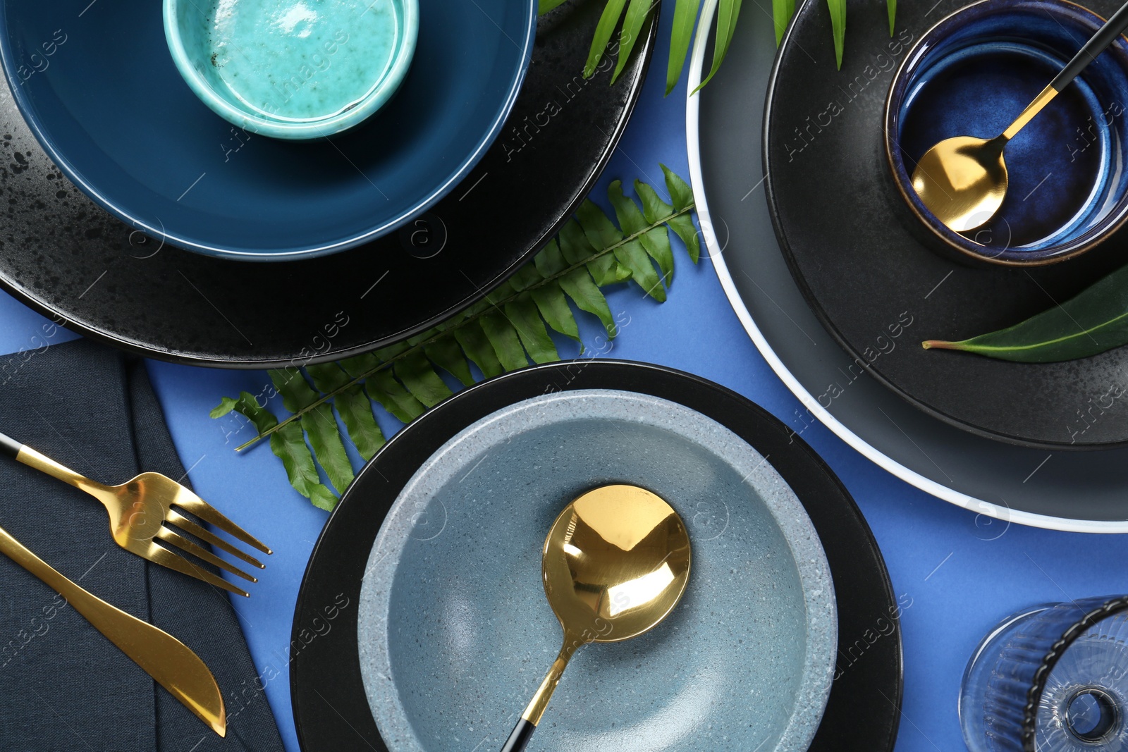 Photo of Flat lay composition with stylish ceramic plates and floral decor on blue background