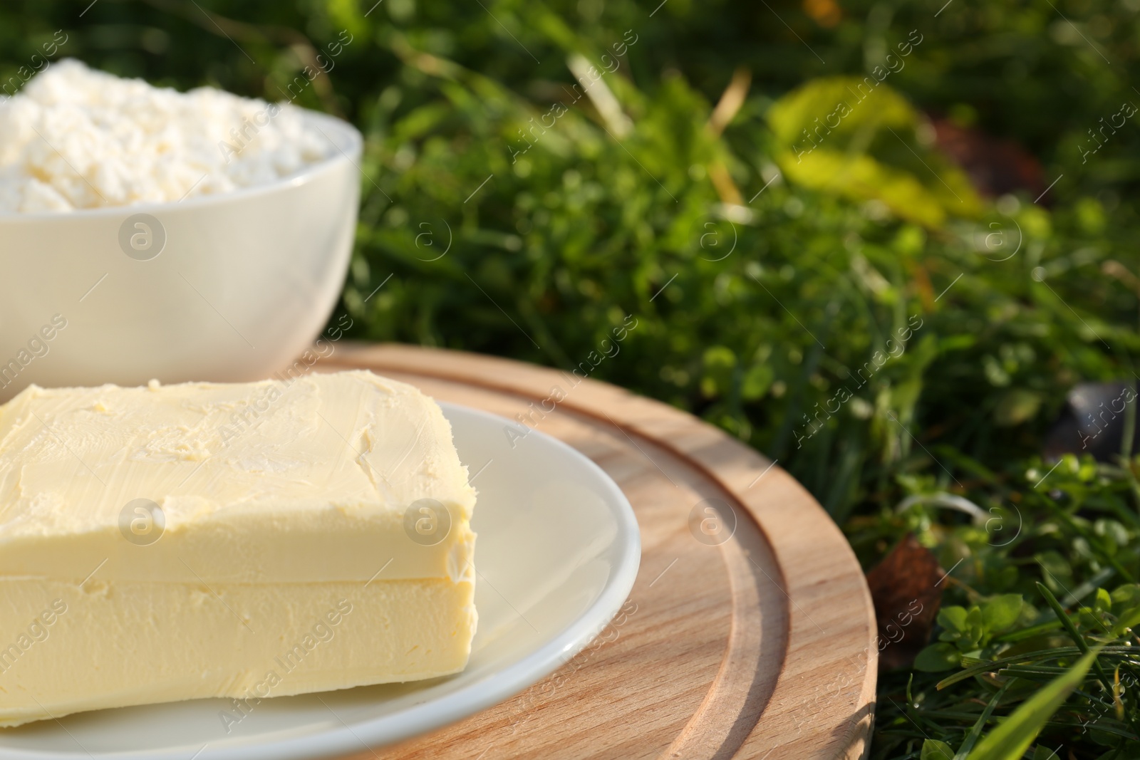 Photo of Wooden tray with tasty homemade butter and dairy products on grass outdoors, closeup. Space for text