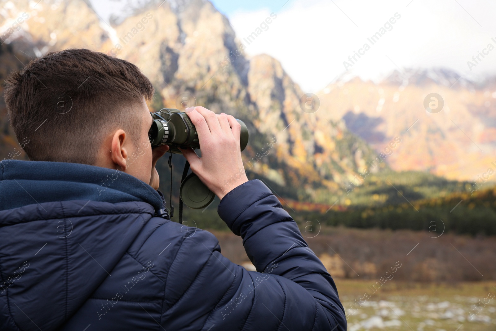 Photo of Boy looking through binoculars in beautiful mountains, back view. Space for text