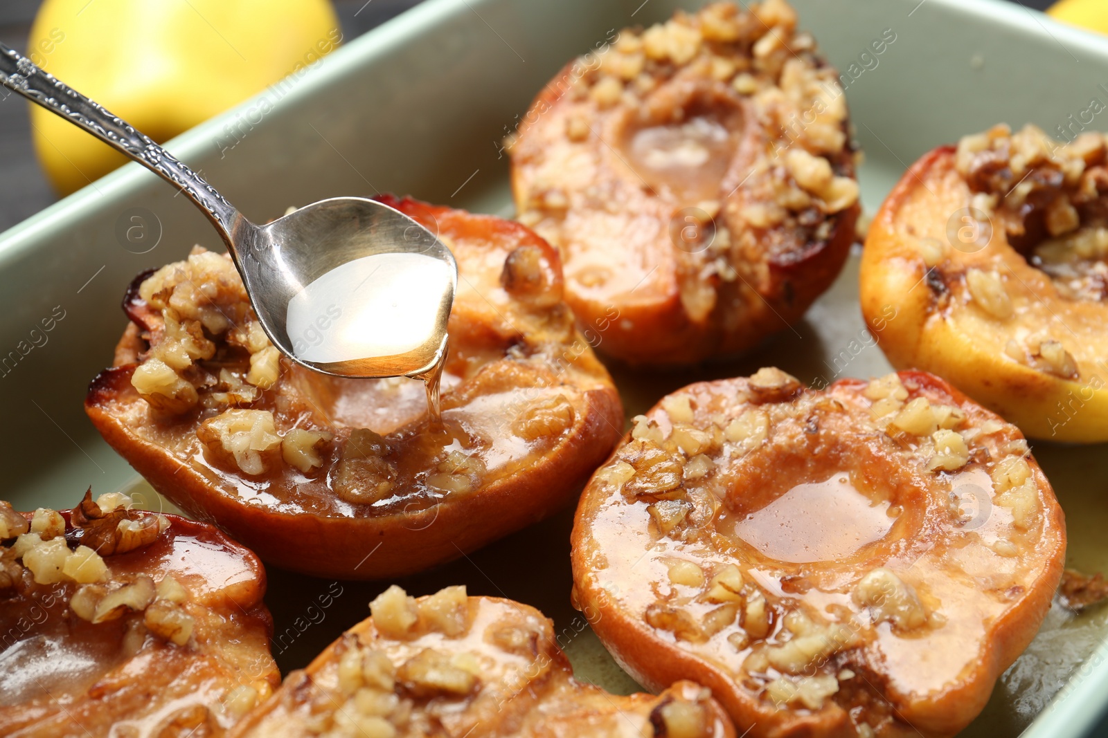 Photo of Pouring honey onto tasty baked quinces with nuts in dish, closeup