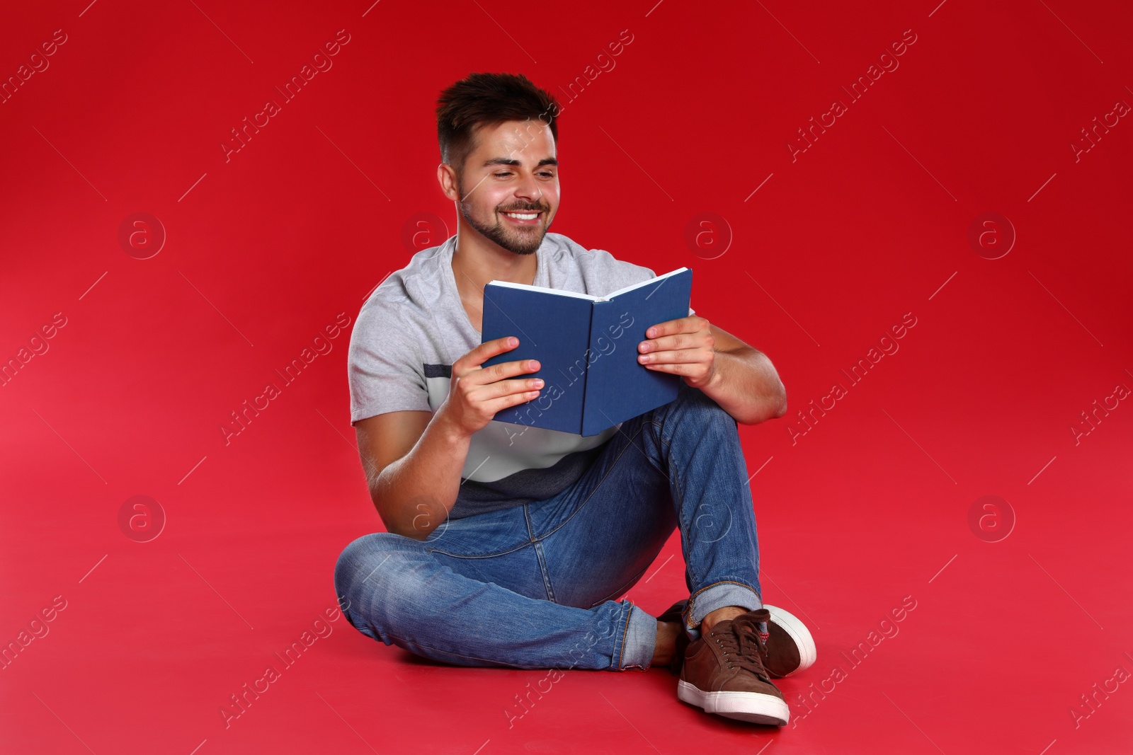 Photo of Handsome young man reading book on red background