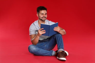 Handsome young man reading book on red background