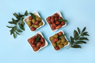 Photo of Different fresh olives and green leaves on light blue background, flat lay