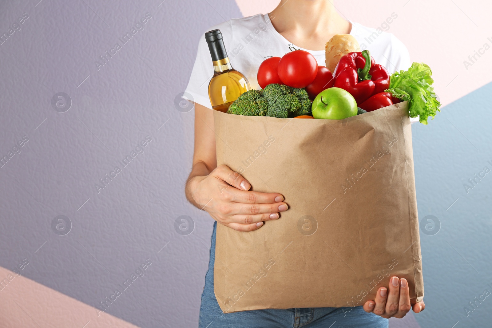 Photo of Woman holding paper bag with different groceries near color wall, closeup view. Space for text