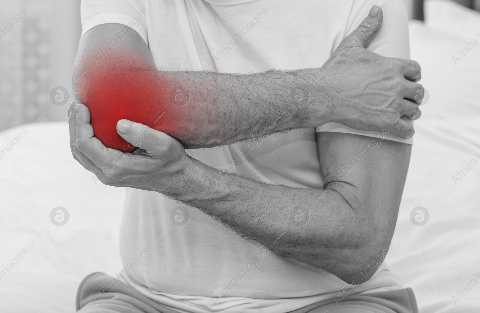 Image of Man suffering from pain in elbow on bed at home, closeup. Black and white effect