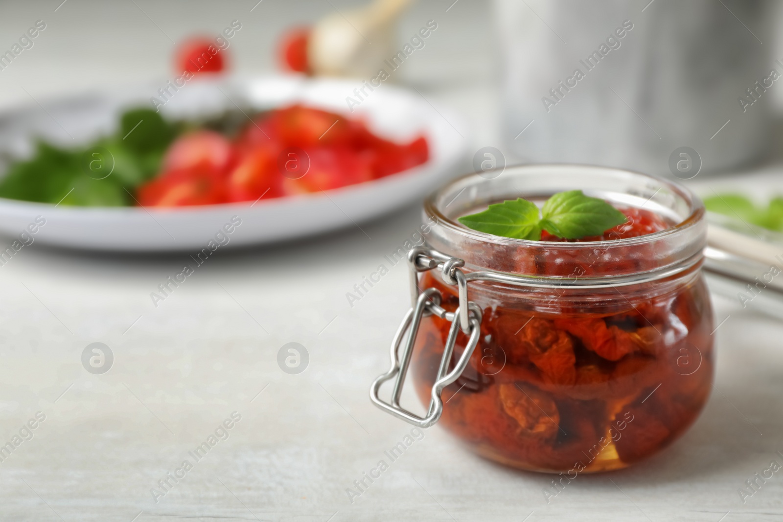 Photo of Jar with sun dried tomatoes on light table. Space for text