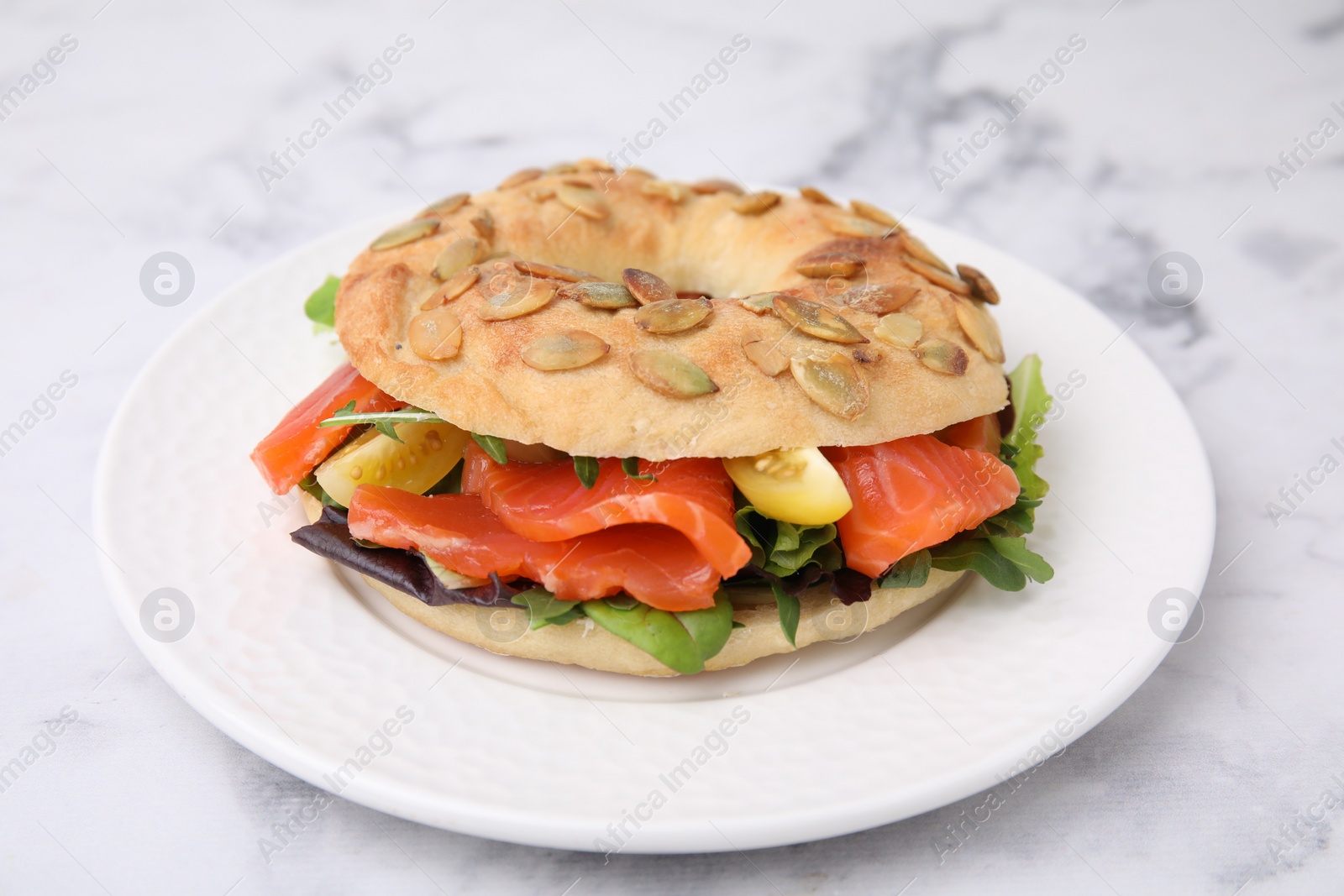 Photo of Tasty bagel with salmon and tomatoes on white marble table, closeup