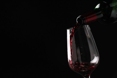 Photo of Pouring tasty red wine from bottle into glass on black background, closeup. Space for text