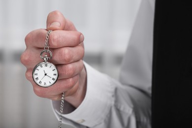 Man holding chain with elegant pocket watch on blurred background, closeup